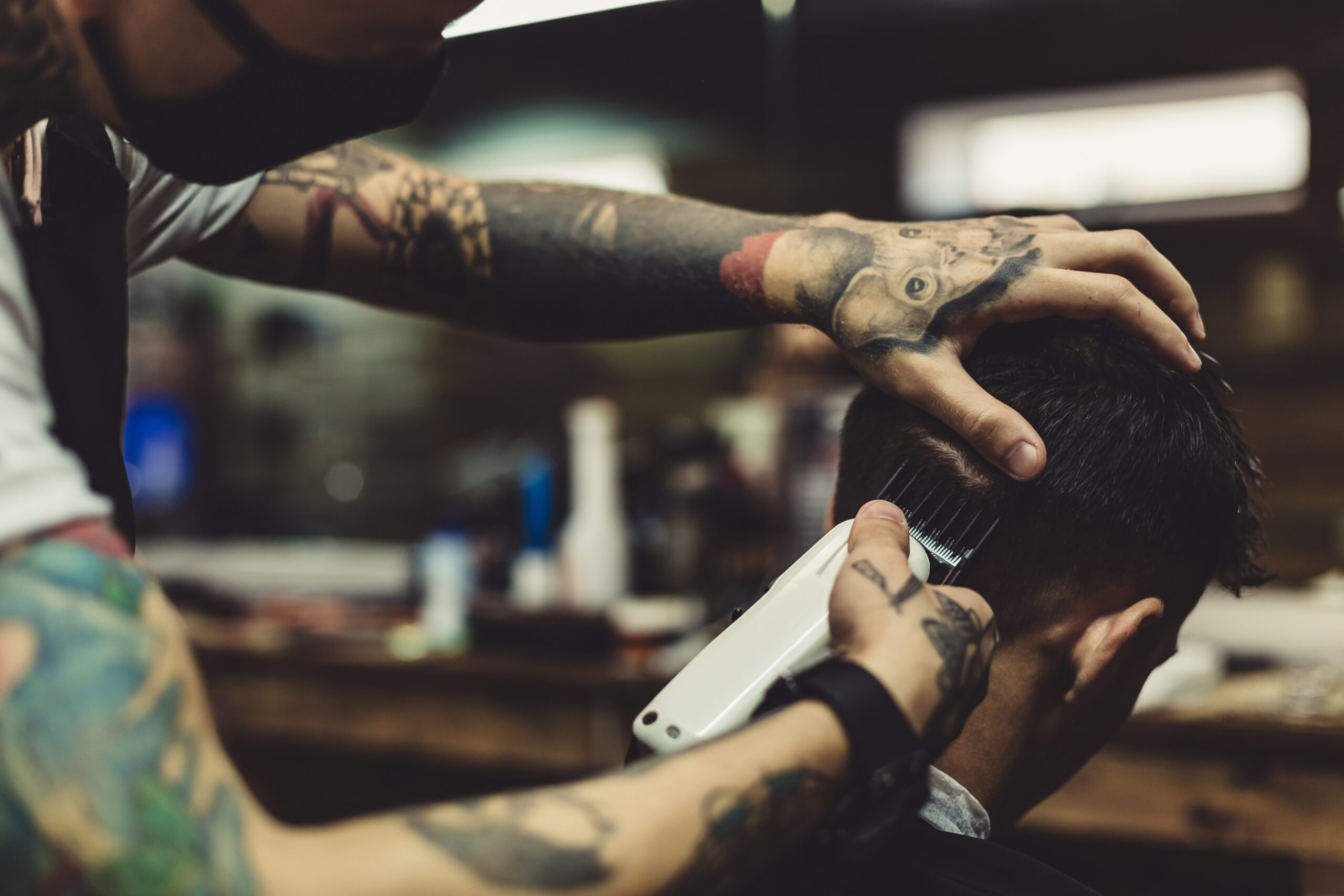 crop-tattooed-stylist-concentrated-shaving-man-with-machine-doing-hairstyle-scaled.jpg